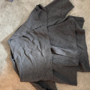 Mörkgrå l kappa i ullmix ZARA - En stilren och lång mörkgrå kappa med rak passform och breda slag. Jackan är tillverkad i mjuk ullmix och har en minimalistisk look utan synliga knappar eller dragkedjor. Perfekt för dig som gillar en clean och klassisk vibe.