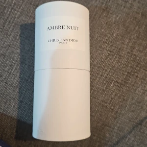 Ambre Nuit Eau de Parfum Dior 125ml - Ambre Nuit från Christian Dior är en lyxig Eau de Parfum i en stilren, genomskinlig glasflaska med svart kork och vit etikett. Doften kommer i en elegant vit kartongtub och innehåller 125 ml. Parfymen har en gyllene färg och exklusiv känsla.