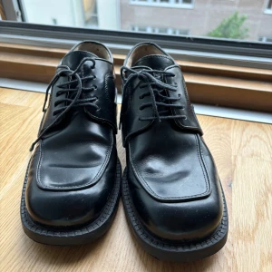 Svarta skinnloafers från Dahlin - Klassiska svarta loafers från Dahlin i äkta skinn med fyrkantig tå och robust sula. Skorna har snörning och stilren design som passar till många olika outfits. Perfekta för dig som gillar en clean och tidlös look.