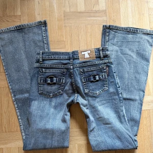 Blå bootcut jeans  - Säljer ett par blå bootcut jeans med snygg tvätt och coola detaljer på bakfickorna. Jeansen har låg midja, klassiska sömmar och breda benslut. Perfekta för dig som gillar en avslappnad men trendig look. Dragkedjan har ramlat av men borde gå att få på igen, annars är jeansen i nytt skick 
