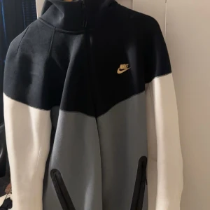 Nike hoodie i svart, grå och vit - Nike tech  hoodie med dragkedja i svart, grått och vitt. Tröjan har huva, långärmade ärmar och två fickor med dragkedja. Perfekt för en sportig och avslappnad stil. Köpt för 1199 SEK 