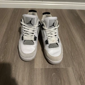 Nike Air Jordan 4 Retro Vit/Svart - Säljer ett par Nike Air Jordan 4 Retro i vitt och svart med coola meshdetaljer och klassisk Jumpman-logga på plösen. Skorna har snörning, platt sula och paneler i både skinn och mocka. Perfekta för dig som gillar streetstyle och vill sticka ut. Om köperen kan vi skicka in dom på tvättning. 