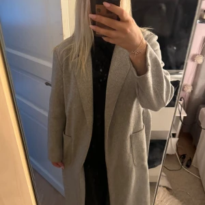 Ljusgrå kappa från ONLY - Säljer min ljusgrå kappa från ONLY i storlek M. Kappan har klassisk krage, stora fickor framtill och medföljande bälte i midjan. Perfekt till höst och vinter❄️
