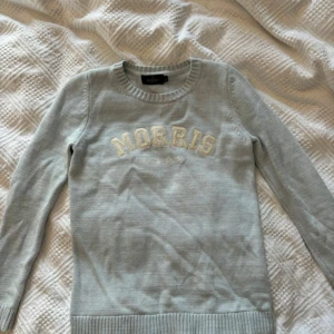 Ljusblå stickad tröja Morris Lady - Supersnygg ljusblå stickad tröja från Morris Lady i 100% bomull. Tröjan har rund hals, ribbade muddar och broderad logga på ärmen. Stor MORRIS-text framtill i vitt. Perfekt för dig som gillar klassisk och clean stil.