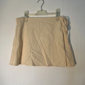 Cremefärgad omlottkjol från Zara - Säljer en cremefärgad kort omlottkjol från Zara i storlek M. Kjolen har en snygg knytning i sidan. Ny med prislapp 