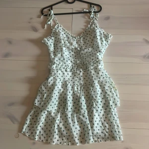 Prickig vit volangklänning Simplee S - Supersöt kort klänning från Simplee i storlek S. Den är vit med gröna prickar, har volanger och knytband på axlarna.