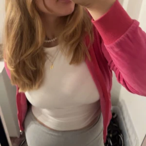 Juicy Couture rosa hoodie i velour - Juicy Couture hoodie i starkt rosa velour med huva och dragkedja. Stor JC-logga i vitt på ryggen omgiven av ett hjärtmönster. Mjukt material och klassisk passform, perfekt för en chill och trendig look.