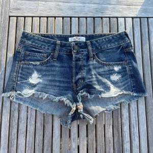 Blå jeansshorts Hollister - Snygga mörkblå jeansshorts från Hollister med slitna detaljer och fransig kant. Perfekta för varma sommardagar.