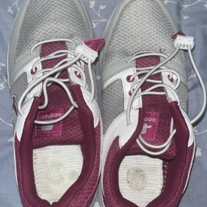 Grå och vinröda sneakers med snörning - Snygga sneakers från Li-Ning i grått och vinrött med vita detaljer. Ovandelen är i mesh och syntet, vilket ger en sportig look och bra andningsförmåga. Skorna har klassisk snörning och en vit sula med mönster. Perfekta för dig som gillar stilrena och bekväma sneakers.