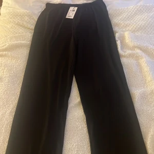 Svarta byxor från 157 - Svarta byxor från lager 157 med elastisk midja och rak passform. Byxorna är enkla och stilrena, perfekta för dig som gillar en clean look. Materialet känns mjukt och bekvämt, vilket gör dem lätta att bära hela dagen. Har alldrig andvänt.