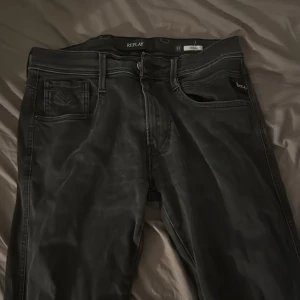 Svarta Replay Anbass jeans herr - Säljer ett par svarta Replay Anbass jeans i klassisk femficksmodell. Jeansen har raka ben, normal passform och snygga detaljer vid fickorna. Materialet är mjukt och stretchigt för extra komfort. Perfekta för dig som gillar stilrena och moderna jeans.