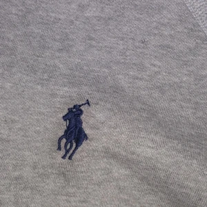 Grå hoodie från Polo Ralph Lauren - Snygg grå hoodie från Polo Ralph Lauren i bomull med dragkedja och huva. Klassisk blå broderad logga på bröstet och custom fit-passform. Perfekt för en chill och stilren look.