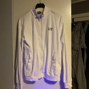 Vit jacka från EA7 Emporio Armani -  vit kofta från EA7 Emporio Armani med dragkedja framtill och två fickor. Har ej själv aldrig använt den men köpt den från en polare, den har någon fläck vid halsen annars är den fin 