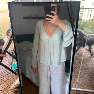 Ljusblå blus med spets från Divided - Supersöt ljusblå blus från Divided med v-ringning, långa ärmar med knyt och transparent spetsdetalj på ryggen. Luftig och flowy passform, perfekt för vår och sommar. Tunt material som ger en romantisk vibe.