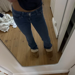 Blå bootcut jeans med broderad ficka  - Säljer ett par blå jeans med bootcut-modell och låg midja från Nelly. Jeansen har klassiska fem fickor och en snygg broderad detalj på bakfickan. Tillverkade i jeansmaterial med stretch för skön passform. Perfekta för dig som gillar en avslappnad men trendig look. Vet ej vilken storlek dessa är i, men jag är 1,67 cm på ett ungefär och som ni ser på bilden är de perfekta i längden (om man föredrar lite längre jeans). Jeansen är använda ett fåtal gånger och har inga ”skador”. Originalpriset är 700