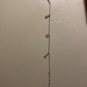Äkta Silver charmarmband med berlocker - Snyggt silver armband med flera små berlocker, bland annat ett hjärta, en hand och en wishbone. Kedjan är tunn och har en cool, ungdomlig vibe. Perfekt för dig som gillar att mixa och matcha smycken och vill ha något personligt på handleden.