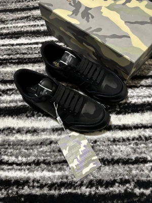 Valentino Garavani Rockrunner sneakers svart - Svarta Valentino Garavani Rockrunner sneakers med snygga kamouflagemönster på ovansidan. Skorna har rund tå, platt sula och snörning. Materialmix av skinn och syntet. Kommer med originalkartong, extra skosnören och dustbag.