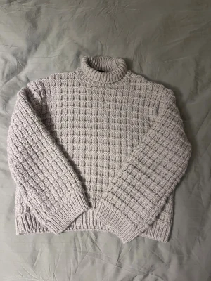 Beige stickad polotröja från H&M - Säljer en beige stickad polotröja från H&M i storlek XS. Tröjan har ett grovt rutmönster, ribbade muddar och hög krage som ger extra mysfaktor. Perfekt för kyliga dagar och enkel att styla med jeans eller kjol.