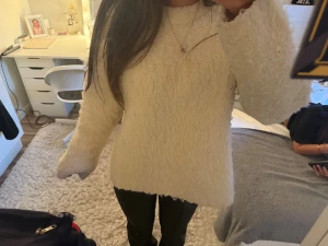 Vit fluffig stickad tröja - Mysig vit stickad tröja med fluffig yta och långärmad modell. Perfekt för kyliga dagar och har en loose passform som ger en avslappnad vibe. Enkel att matcha med både jeans och leggings. Lite makeup på halsen men tröjan ska tvättas o syns knappast❤️☺️🫰🏼😅😅