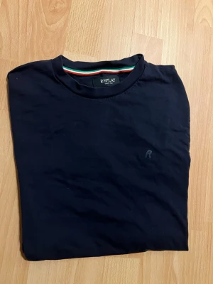 Mörkblå t-shirt från Replay - Snygg mörkblå t-shirt från Replay med diskret logga på bröstet och färgglad randig detalj på insidan av kragen. Klassisk rund hals och korta ärmar. Mjuk och skön bomull som passar perfekt till jeans eller shorts.