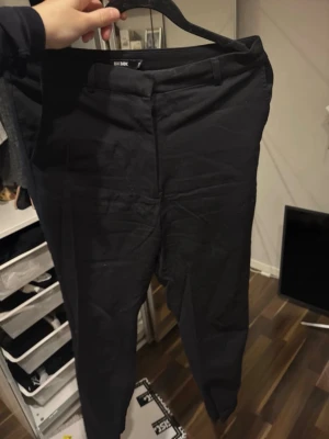 Svarta kostymbyxor från Bik Bok - Snygga svarta kostymbyxor från Bik Bok med smal passform och croppad längd. Byxorna har klassiska fickor bak, bälteshällor och dragkedja vid benslut för extra stil. Perfekta för dig som gillar en clean och modern look.