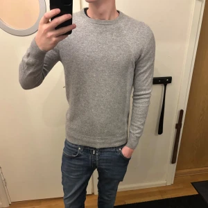 Grå kashmirtröja från Bläck, M - Snygg grå tröja från Bläck i 100% kashmir. Klassisk rund hals och ribbade muddar vid ärmslut och nederkant. Långärmad och med en normal passform som sitter skönt. Perfekt för dig som gillar stilrena och mjuka plagg.