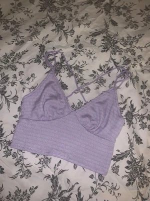 Ljuslila croppad linnetopp - Säljer en ljuslila croppad topp från shein med smala axelband som korsas i ryggen. Toppen har en ribbad struktur och är ärmlös med v-ringad front. Perfekt för dig som gillar en enkel men snygg look med lite extra färg.