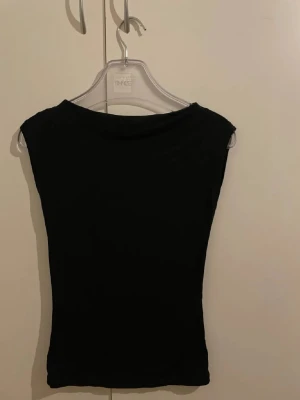 Svart ärmlös topp från Nelly  - Säljer en enkel svart topp med ärmlös design och rund hals. Perfekt att matcha med jeans eller kjol för en clean look. Materialet känns mjukt och stretchigt, vilket gör den bekväm att bära hela dagen.