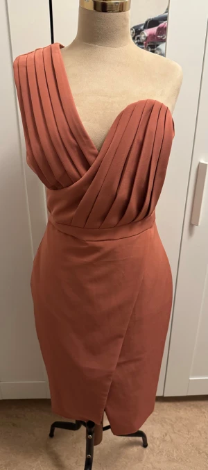 Rostfärgad omlottklänning Lavish Alice - Snygg rostfärgad kortklänning från Lavish Alice med omlottdesign och plisserad v-ringad överdel. Klänningen har oneshoulder och figurnära passform, tillverkad i ett mjukt syntetmaterial. Dragkedja i ryggen för enkel påklädning. Perfekt för dig som gillar stilrena detaljer.