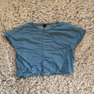  Blå loose topp från Lindex - Säljer en blå loose topp från Lindex i storlek M. Toppen har korta ärmar, rund halsringning och är tillverkad i mjuk bomull. Perfekt för en avslappnad stil och enkel att matcha med jeans eller shorts.  Den är i jeans färg men inte i jeans material. Den är inte stretchig.  Den har en liten fläck som troligen går bort i tvätten. Material: 100% lyocell Storlek M Från Lindex