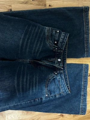Mörkblå wide jeans med slitningar - Snygga mörkblå jeans med breda ben och coola slitningar över låren. Klassisk femficksmodell med knapp och dragkedja i midjan. Perfekta för dig som gillar en avslappnad och trendig stil.
