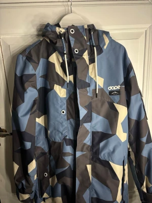 Dope camo vindjacka med huva - Säljer en fet vindjacka från Dope med blått, beige och mörkgrått camouflagemönster. Jackan har huva med snörning, dragkedja och flera fickor. Perfekt för dig som gillar streetstyle och vill sticka ut med cool design.