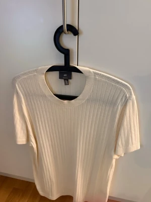 Ribbad vit t-shirt  - Säljer en ribbad vit t-shirt från H&M med rund hals och korta ärmar. Tröjan har en clean och stilren look med vertikala ribbade ränder som ger lite extra struktur. Perfekt för dig som gillar enkel och snygg stil.