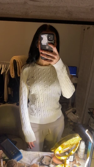 Vit stickad tröja från Gant - Vit stickad tröja från Gant med rund hals och diskret logga broderad på bröstet. Tröjan har långärmade ribbade muddar och är gjord i mjuk bomull. Snygg passform som sitter normalt och passar perfekt till jeans eller chinos.