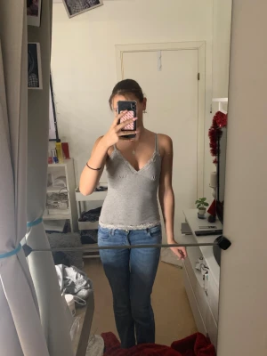 Grå linnetopp med spetskant🩶 - Säljer en grå linnetopp med smala axelband och v-ringad hals. Toppen har fina spetsdetaljer i vitt längs halsringningen och nederkanten. Mjuk och stretchig bomull som sitter tight och är perfekt för varma dagar.💖