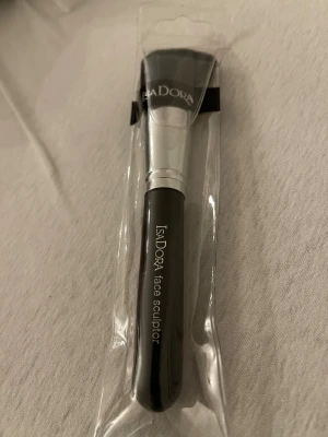 Isadora Face Sculptor sminkborste - Sminkborste från Isadora, Face Sculptor, med svart handtag och silverfärgad metall vid borsthuvudet. Borsten är tät och mjuk, perfekt för contouring och applicering av bronzer eller highlighter. Kommer i originalförpackning.