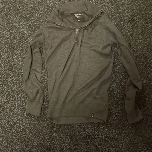 Mörkgrå långärmad tröja Indicode - Säljer en mörkgrå långärmad tröja från Indicode i storlek small. Tröjan har en hög krage med half zip-dragkedja och är tillverkad i mjukt material som känns skönt mot huden. Perfekt för lager-på-lager under kyliga dagar.