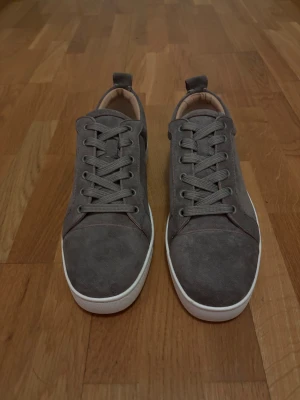 Christian Louboutin - Snygga grå sneakers med vit platt sula och rund tå. Skorna har snörning och beige innersida, vilket ger en clean och stilren look. Perfekta för dig som gillar enkel design och neutrala färger.