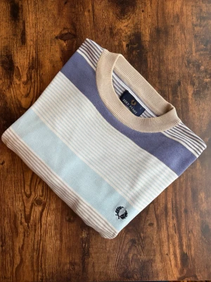 Fred Perry Tröja - Fred Perry tröja i klassisk casuals/old money-stil. Välvårdad och i bra skick utan hål, fläckar eller slitage. Tidlös design med diskret logotyp, stark koppling till brittisk casuals-kultur. Perfekt både till vardag och mer uppklädda outfits. Ett stilrent plagg som aldrig går ur tiden.