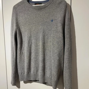 Grå stickad tröja från Morris - Snygg grå stickad tröja från Morris i storlek L. Men rätt liten i storleken så passar bra till M Tröjan har rund hals, ribbade muddar och en liten blå broderad logga på bröstet.                             Skriv vid minsta fundering!🍾💫