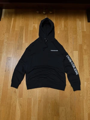 Calvin Klein Jeans Hoodie – Svart - Stilren svart hoodie från Calvin Klein Jeans med logga på ärmen och bröstet. Mjuk, bekväm och i mycket gott skick. Huva och magficka.