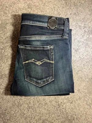 Mörkblå replay jeans W27 L32 - Säljer ett par mörkblå skinny jeans från Replay med snygga slitningar och kontrastsömmar. Klassisk femficksmodell med Replay-logga på bakfickan och patch i midjan. Jeansen har smal passform och är tillverkade i stretchig jeansbomull för extra komfort.