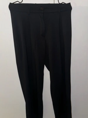 Svarta kostymbyxor från Nelly - Snygga svarta kostymbyxor från Nelly i storlek S. Byxorna har klassisk rak passform med pressveck och midjehöjd med knappstängning. Perfekta för en clean och stilren look. Materialet känns mjukt och har en lätt stretch för extra komfort.