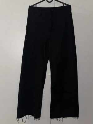 Svarta wide jeans från Zara, strl 40 - Svarta jeans från Zara i storlek 40 med breda ben och råa, fransiga kanter nedtill. Klassisk femficksmodell med hög midja och raka bakfickor. Materialet är jeans och byxorna har en loose passform som ger en chill vibe.