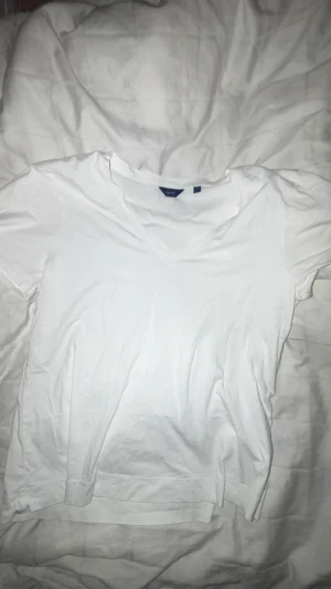 Vit v-ringad t-shirt från GANT - Säljer en vit t-shirt från GANT i storlek M. T-shirten har v-ringad hals och korta ärmar, med en diskret broderad GANT-logga på bröstet. Tillverkad i mjuk bomull som känns skön mot huden och har en klassisk, normal passform.