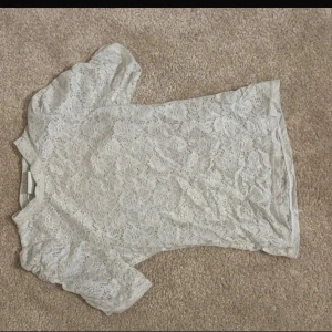 Vit spetsblus med puffärm - Säljer en vit blus i spets med kort puffärm och rund hals. Blusen har ett romantiskt blommigt spetsmönster och är lätt transparent. Perfekt för dig som gillar feminina detaljer och vill ha en topp som sticker ut lite extra.