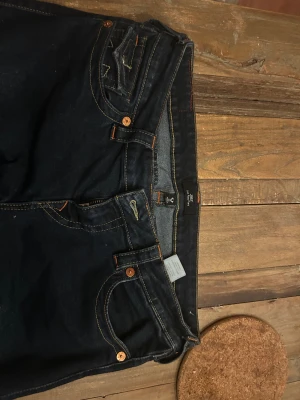 Mörkblå True Religion jeans bootcut - Strl 29, 80 i midje mått och 80 cm i innerbenslängden. Har klippt av dom så de skulle passa min längd 165 cm men annars fint skick.