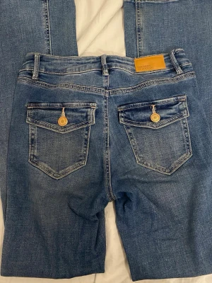 Blå bootcut jeans från Vero Moda - Snygga blå bootcut jeans från Vero Moda med klassisk femficksdesign och gylf med dragkedja. Jeansen har en lätt tvättad look och är tillverkade i stretchigt denimtyg för extra komfort. Katt finns i hemmet!