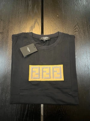 Svart Fendi t-shirt med logga - Snygg svart t-shirt från Fendi med ikonisk broderad logga i gult och grått på bröstet. Klassisk rund halsringning och korta ärmar. Tillverkad i mjuk bomull för skön känsla och stilren look.