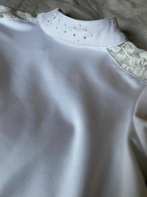 Vit tävlingstopp med spets och pärldetaljer - Supersnygg och söt tävlingstopp från CRW, gjort av skönt marial och har fina detaljer på sig. Denna topp är helt oanvänd och är i storlek 122-128. 💗